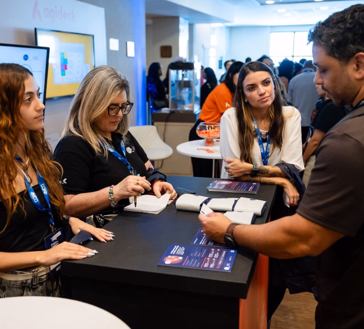 Participantes conversando con un expositor alrededor de una mesa en el área de stands