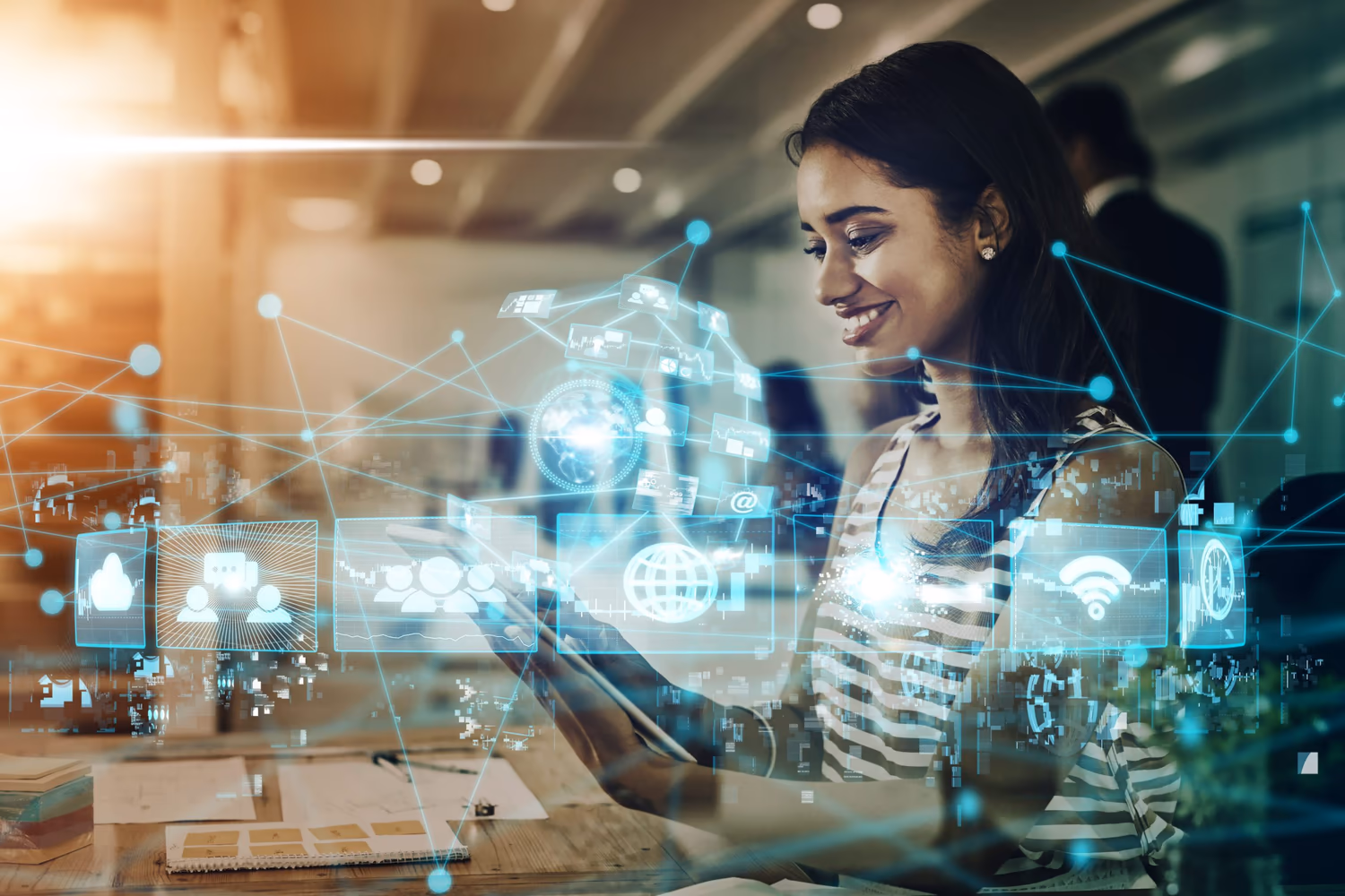 Imagen de una mujer sonriendo mientras utiliza una tablet. Frente a ella se proyectan elementos visuales digitales, como íconos de red, conectividad, nube, gráficos y símbolos globales, que representan la transformación digital. Al fondo, un entorno de trabajo iluminado con otros profesionales alrededor sugiere innovación y productividad en el contexto de la era digital.