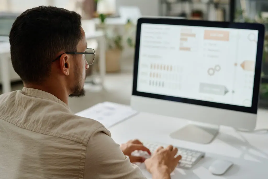 Profissional analisando dados na tela de um computador, com gráficos e indicadores, em um ambiente moderno. Ele está focado em processos relacionados a MDM (Master Data Management), uma área essencial para a otimização e governança de dados, como as soluções oferecidas pela 4MDG.